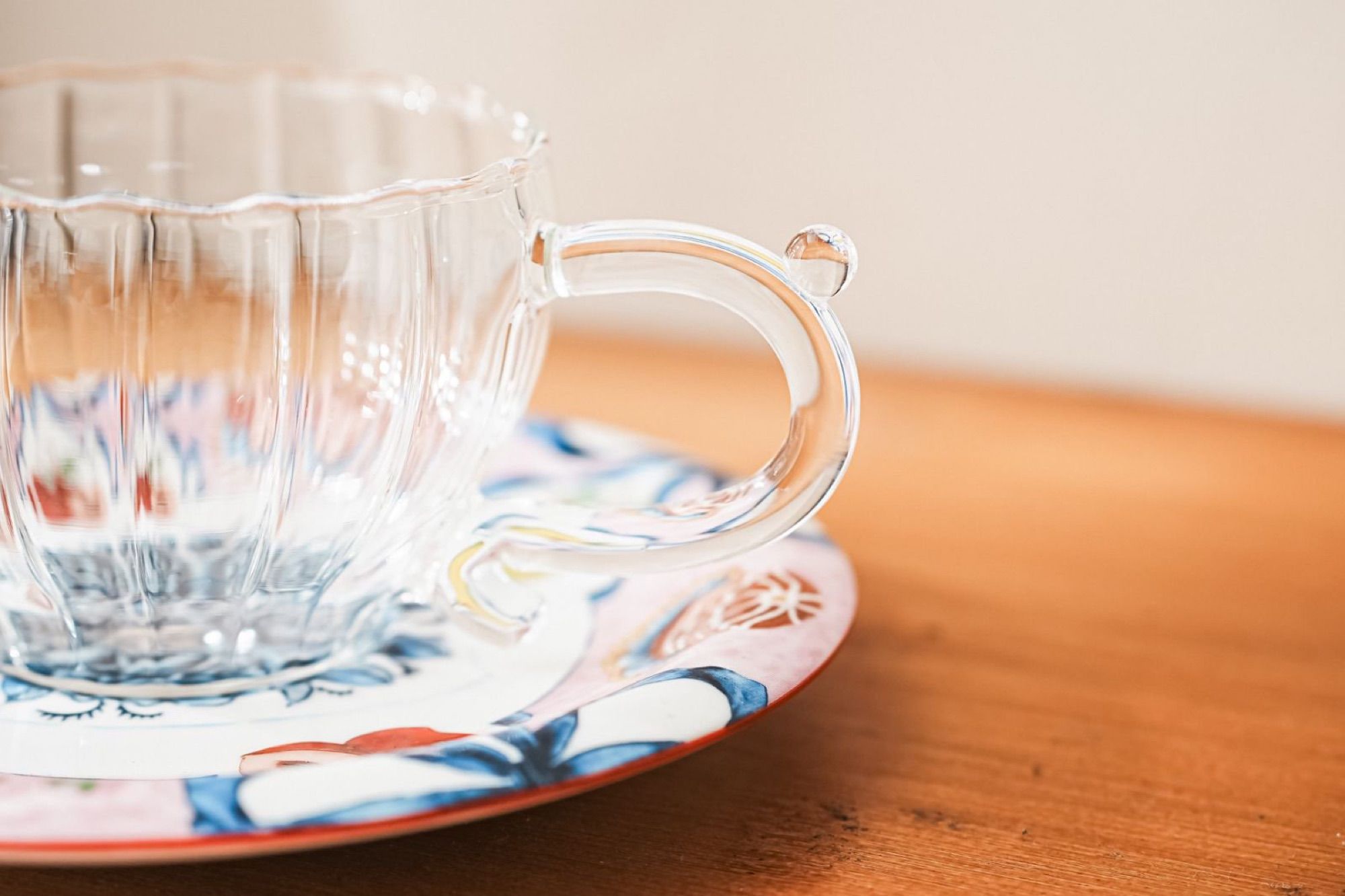 Clear ribbed glass cup standing on a decorated ceramic saucer on a warm wooden surface.