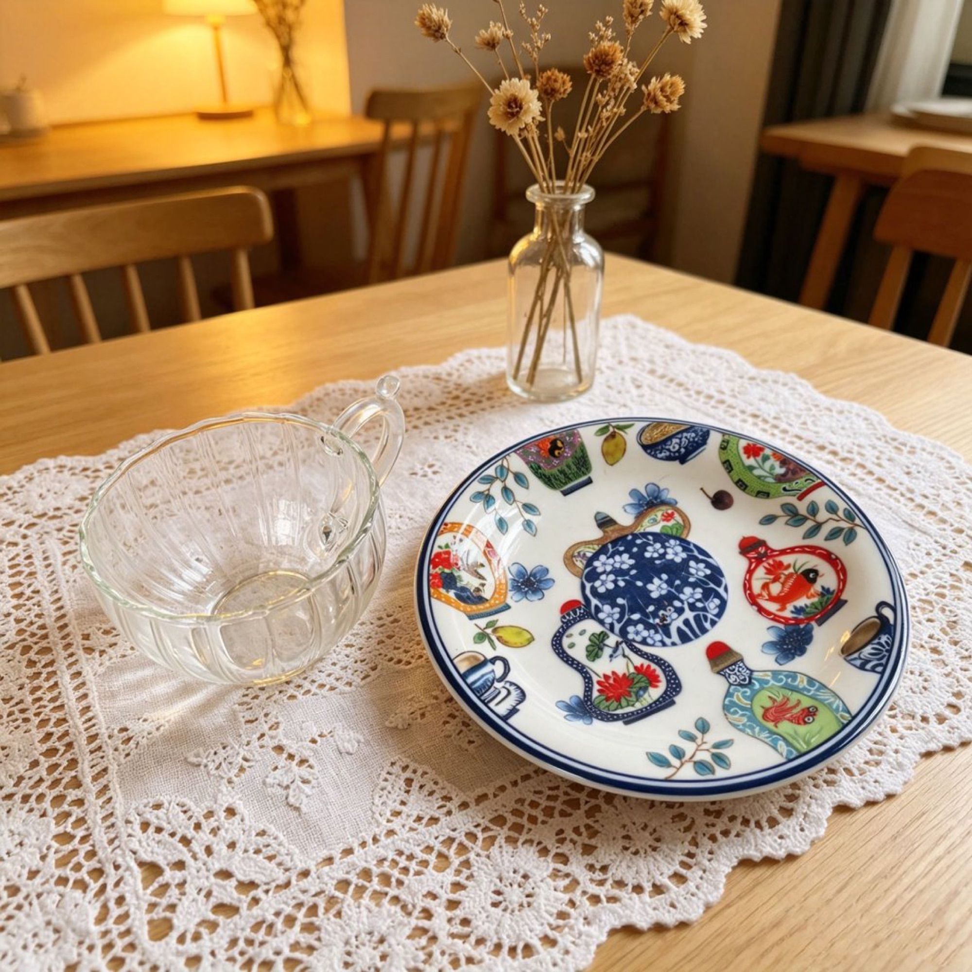 Glass cup and patterned ceramic saucer on a white linen tablecloth with dried flowers.