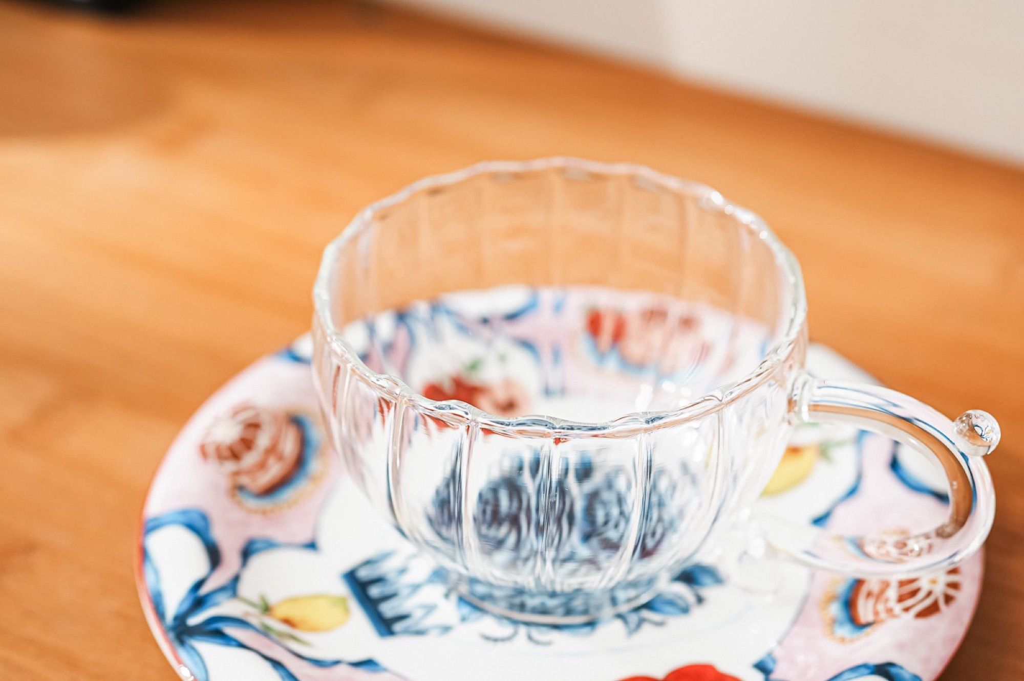 The glass cup and patterned ceramic saucer in low morning light on a wooden table.