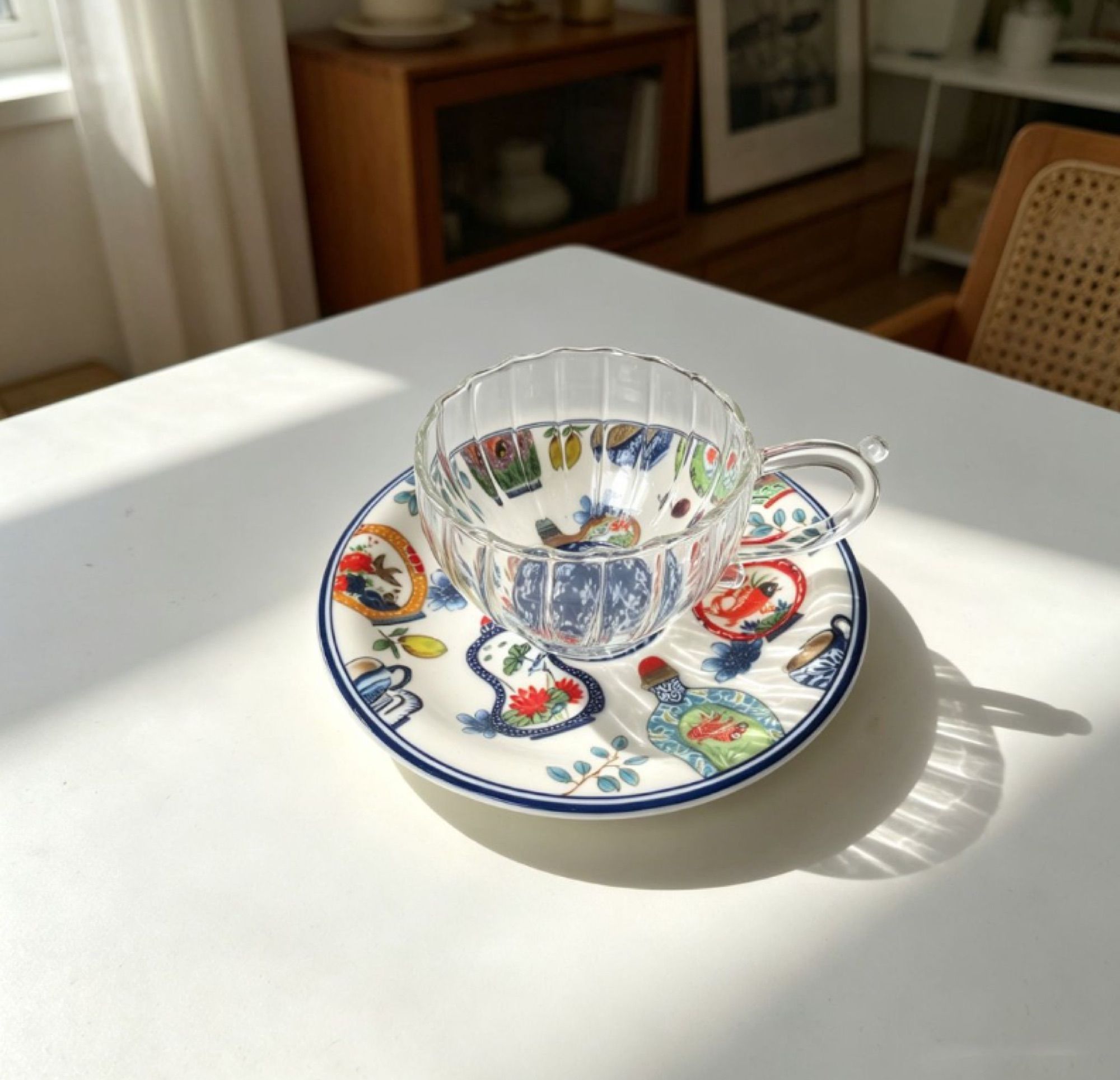 Glass cup and ceramic saucer on a white table, fully lit by direct sunlight.